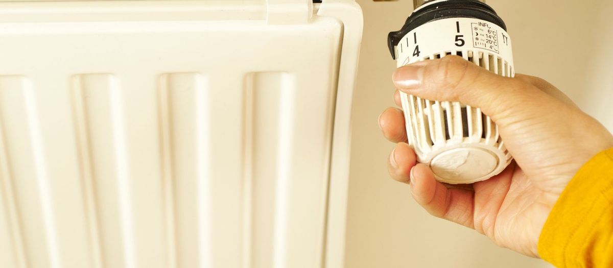 Ręka ustawia głowicę termostatyczną na grzejniku