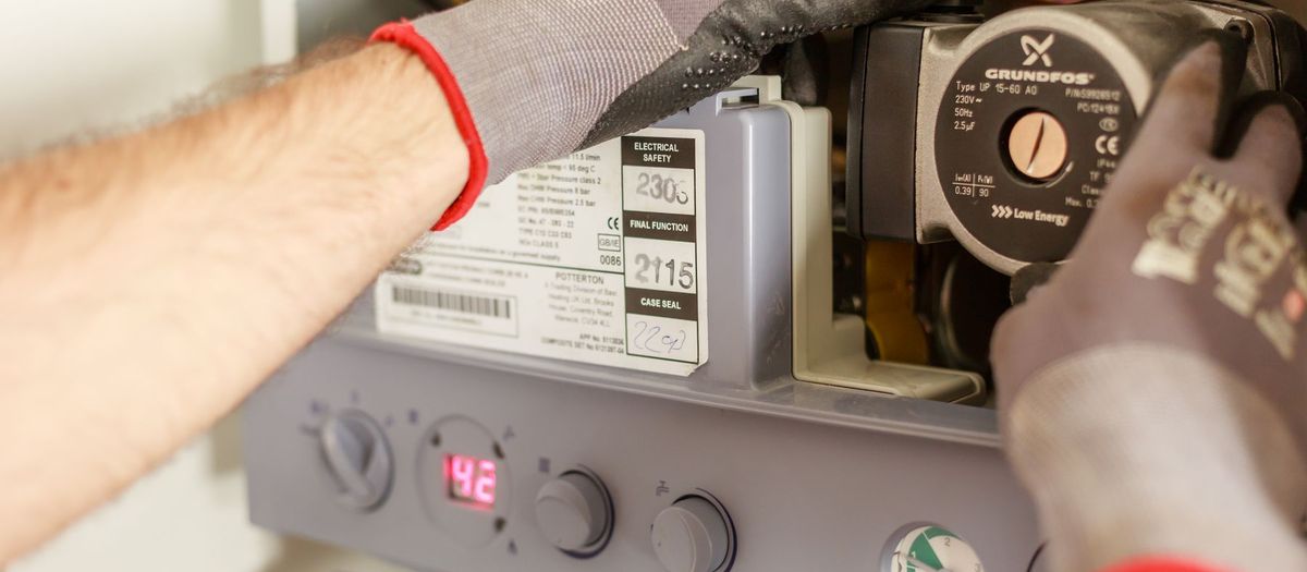 Instalator w rękawicach przy pompie obiegowej kotła